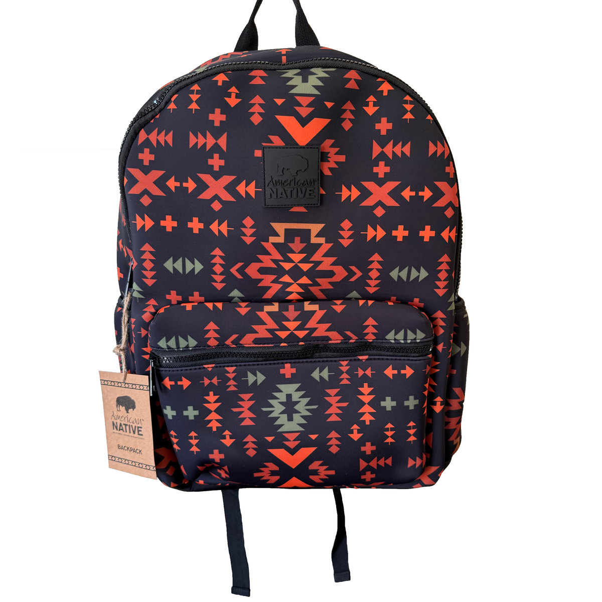 A backpack with a dark navy blue base featuring a vibrant geometric Southwestern pattern in orange, red, and sage green. It has a front zippered pocket, black top handles, and a hanging paper tag on the left side.