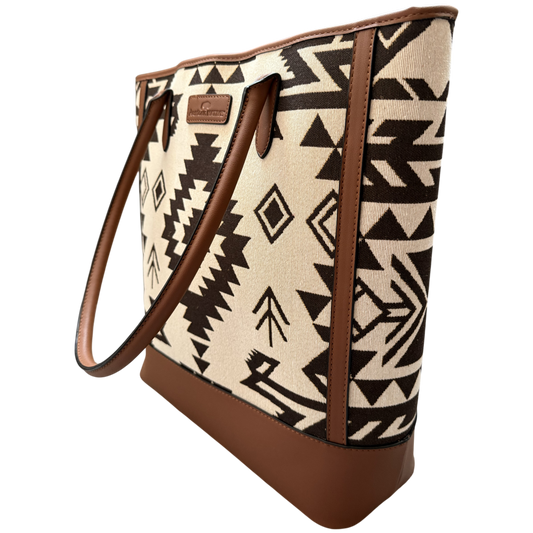 A tote bag with a Southwestern geometric pattern in beige and black, featuring brown faux-leather trim, handles, and base, shown on a plain white background.