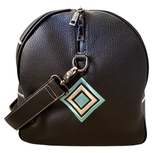 A black pebbled leather duffel bag with a silver zipper, a matching shoulder strap, and a geometric diamond-shaped metal charm in green, beige, and white, shown against a plain white background.