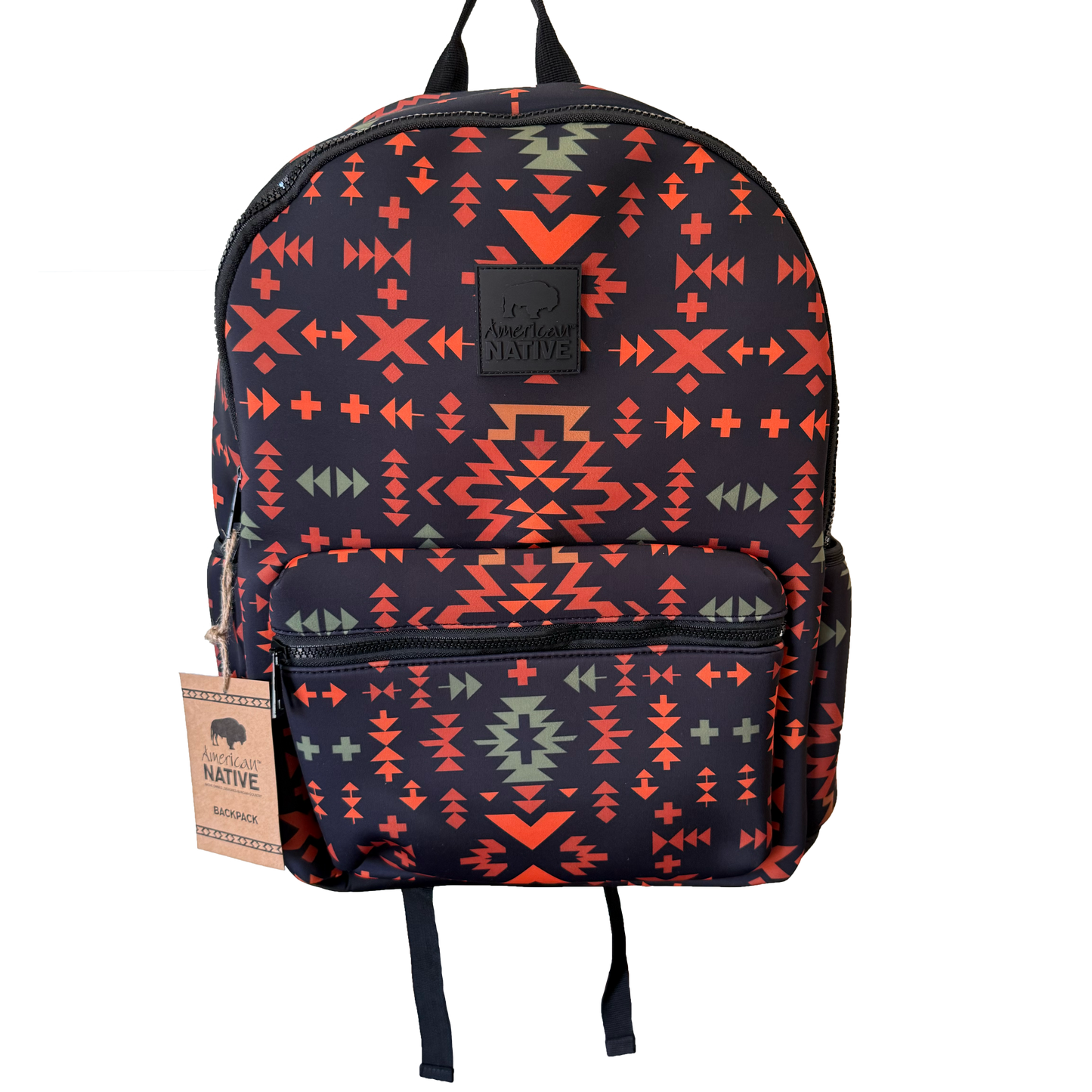 A backpack with a dark navy blue base featuring a vibrant geometric Southwestern pattern in orange, red, and sage green. It has a front zippered pocket, black top handles, and a hanging paper tag on the left side.