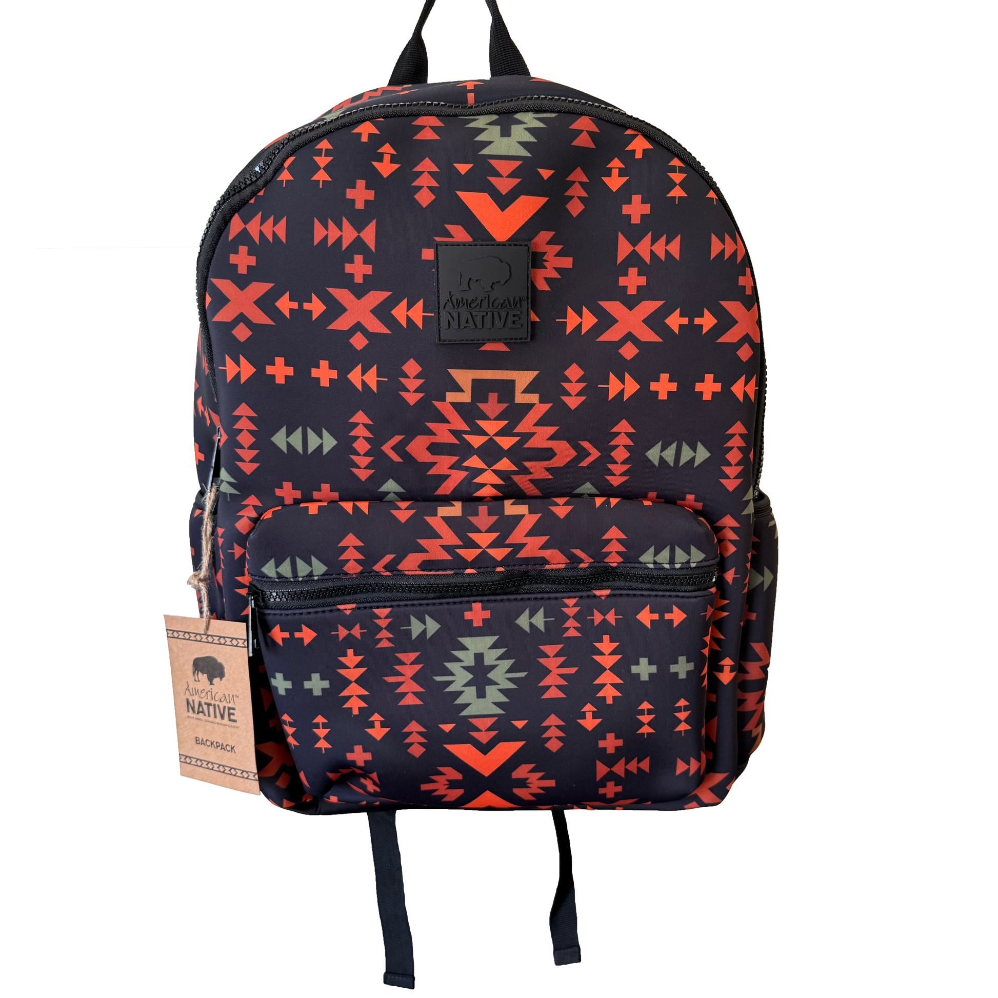 A backpack with a dark navy blue base featuring a vibrant geometric Southwestern pattern in orange, red, and sage green. It has a front zippered pocket, black top handles, and a hanging paper tag on the left side.