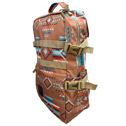 A backpack with a Southwestern geometric pattern in terracotta, blue, orange, and white, featuring tan webbing straps and plastic buckles, shown on a plain white background.