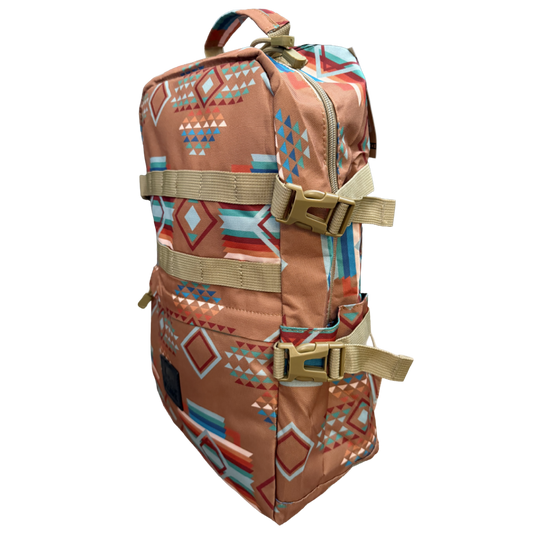 A backpack with a Southwestern geometric pattern in terracotta, blue, orange, and white, featuring tan webbing straps and plastic buckles, shown on a plain white background.