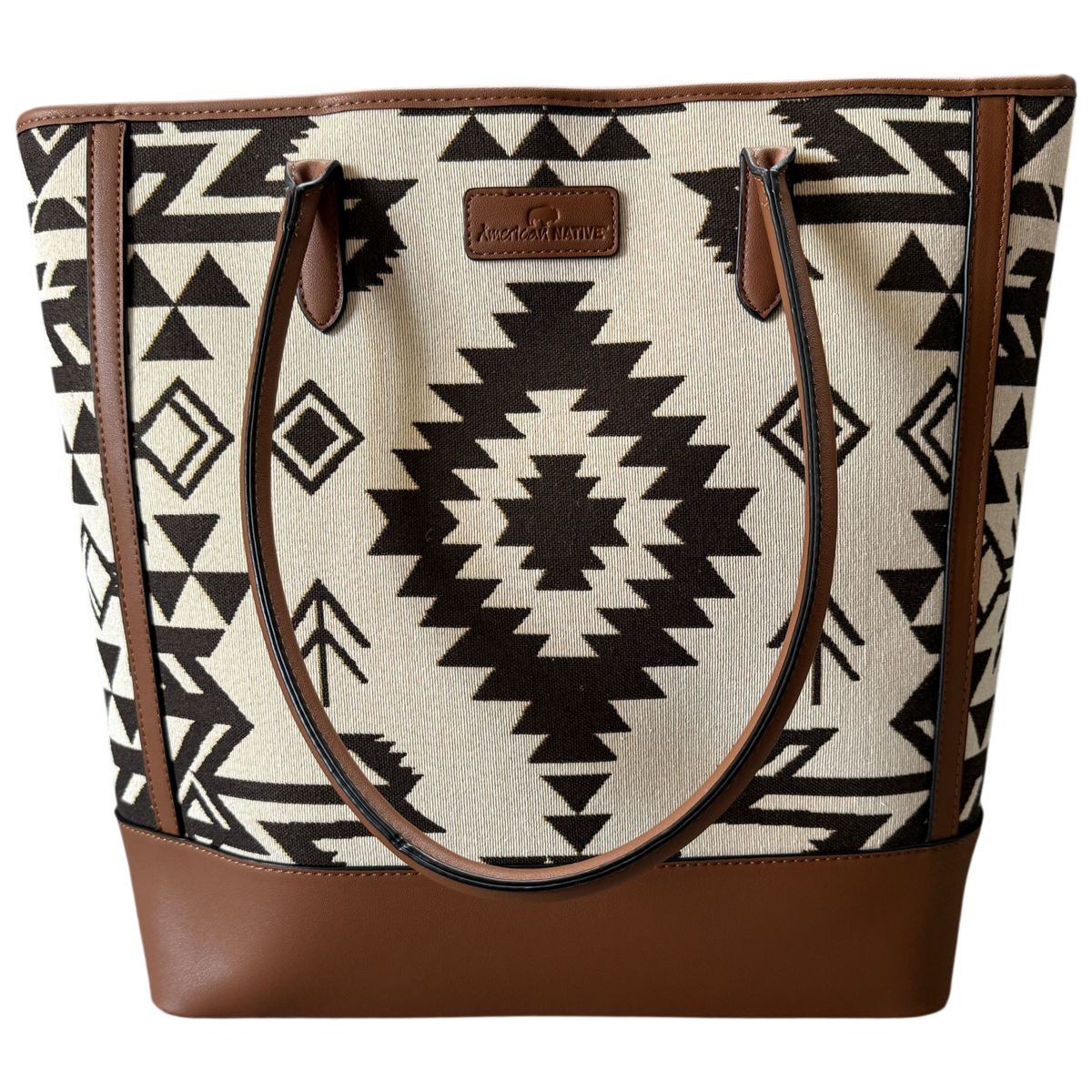 A tote bag featuring a Southwestern geometric pattern in black and cream, with brown faux-leather trim, handles, and base, and a central brand patch.