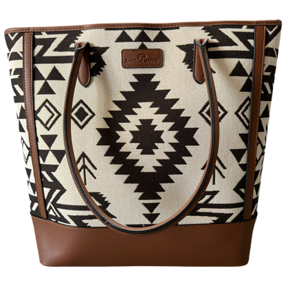 A tote bag featuring a Southwestern geometric pattern in black and cream, with brown faux-leather trim, handles, and base, and a central brand patch.