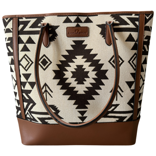 A tote bag featuring a Southwestern geometric pattern in black and cream, with brown faux-leather trim, handles, and base, and a central brand patch.