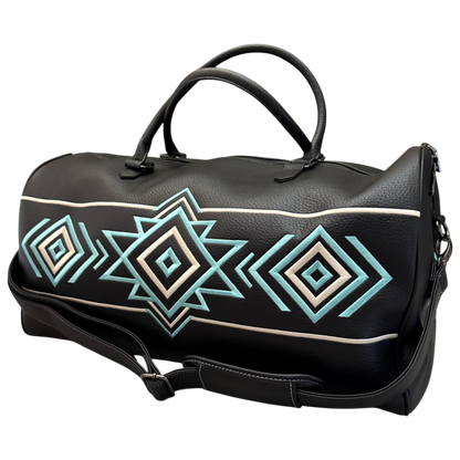 A black faux-leather duffel bag with a geometric Southwestern-style diamond pattern in turquoise, cream, and white, featuring dual top handles and a detachable shoulder strap.