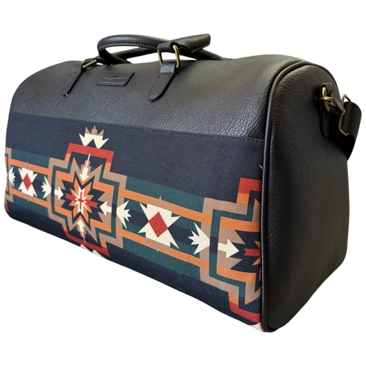 A black pebbled leather duffel bag featuring a Southwestern geometric patterned fabric panel on the front, with dark handles and gold-tone hardware, shown against a plain white background.