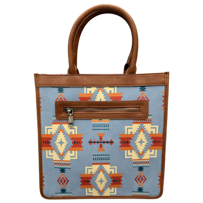A structured tote bag with a light blue fabric body featuring a Southwestern geometric pattern in orange, red, beige, and dark blue. It has brown faux-leather trim, double top handles, and a zippered front pocket.