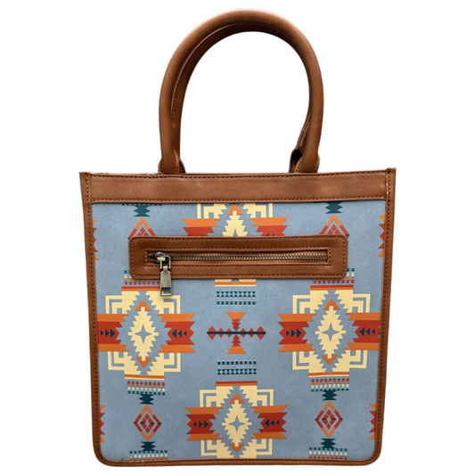 A structured tote bag with a light blue fabric body featuring a Southwestern geometric pattern in orange, red, beige, and dark blue. It has brown faux-leather trim, double top handles, and a zippered front pocket.