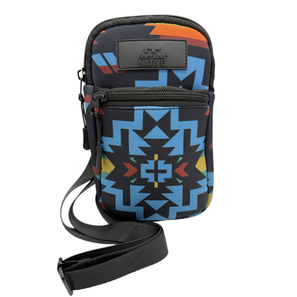 A small crossbody phone bag with a black strap, featuring a colorful geometric Southwestern pattern in blue, orange, yellow, and red on a black background. It has a black leather brand patch on the front that reads 'Lone Star Native'.