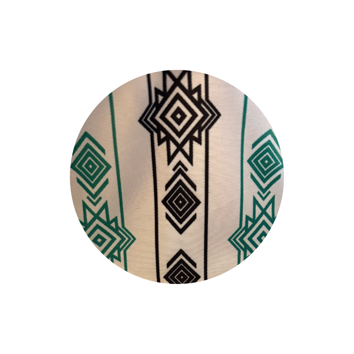 A circular close-up of a patterned textile featuring a cream background with black geometric diamond motifs and green geometric accents.