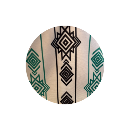 A circular close-up of a patterned textile featuring a cream background with black geometric diamond motifs and green geometric accents.