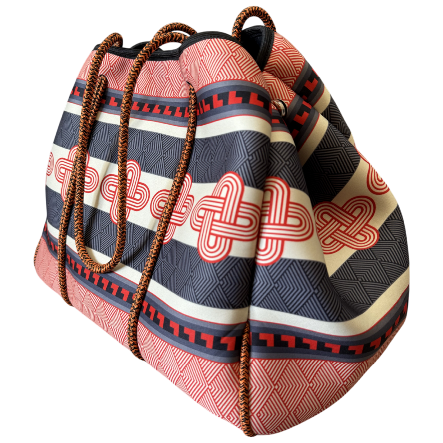 A patterned bucket-style tote bag with woven brown rope handles, featuring horizontal stripes in red, black, and cream with red geometric and knot-like motifs, shown on a plain white background.