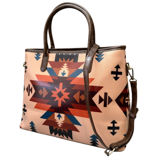 A structured tote bag featuring a Southwestern geometric pattern in terracotta, navy, and black on a light peach-beige background, with dark brown leather handles and trim.
