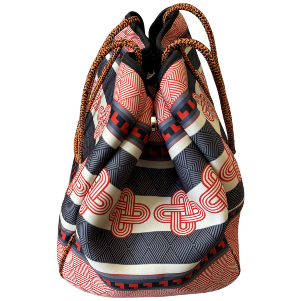 A patterned drawstring bucket bag with a black, beige, and red geometric print, featuring braided brown rope handles, shown against a plain white background.