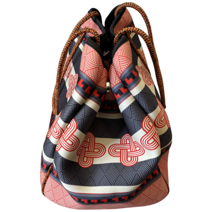 A patterned drawstring bucket bag with a black, beige, and red geometric print, featuring braided brown rope handles, shown against a plain white background.