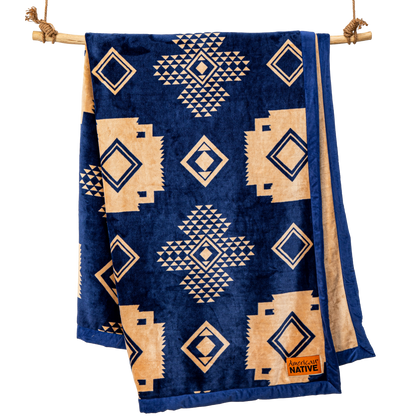 Navy blue blanket with beige geometric patterns hanging on a wooden rod.