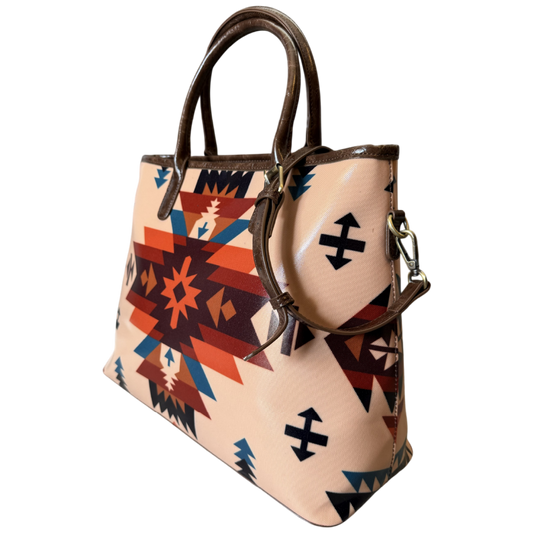 A structured tote bag with a Southwestern geometric pattern in beige, orange, red, brown, and blue, featuring dark brown leather handles and trim, shown against a plain white background.