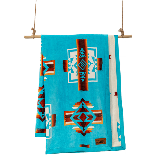 Turquoise blanket with geometric patterns hanging on a wooden rod 