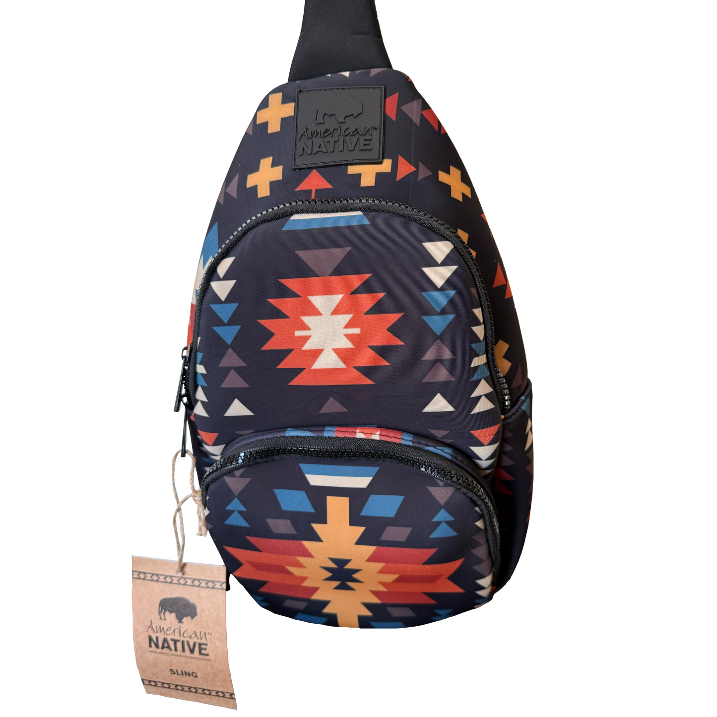A sling backpack with a Southwestern geometric pattern in navy, red, orange, yellow, and white, featuring a black brand patch and a hanging paper tag.