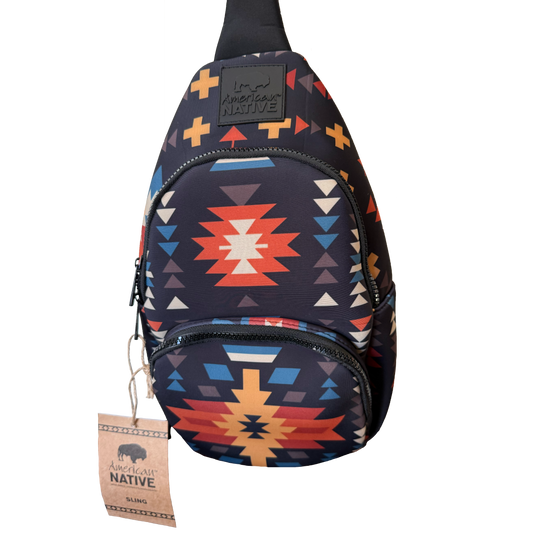 A sling backpack with a Southwestern geometric pattern in navy, red, orange, yellow, and white, featuring a black brand patch and a hanging paper tag.
