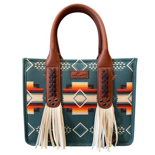 A structured tote bag with a Southwestern geometric pattern in teal, brown, orange, and cream, featuring brown faux-leather handles and long cream tassels.